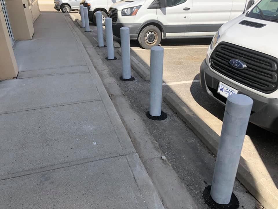 A row of white vans are parked in a parking lot next to a sidewalk.