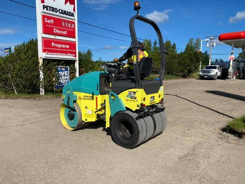 A man is driving a road roller in front of a petro canada gas station