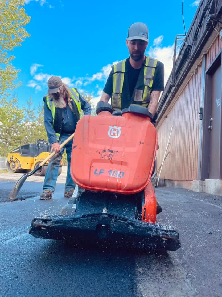A man is riding a lawn mower while another man stands behind him.