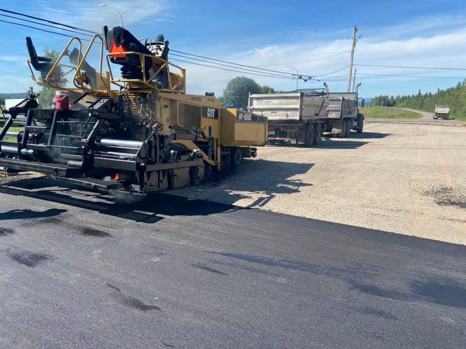 A machine is laying asphalt on a road next to a dump truck.