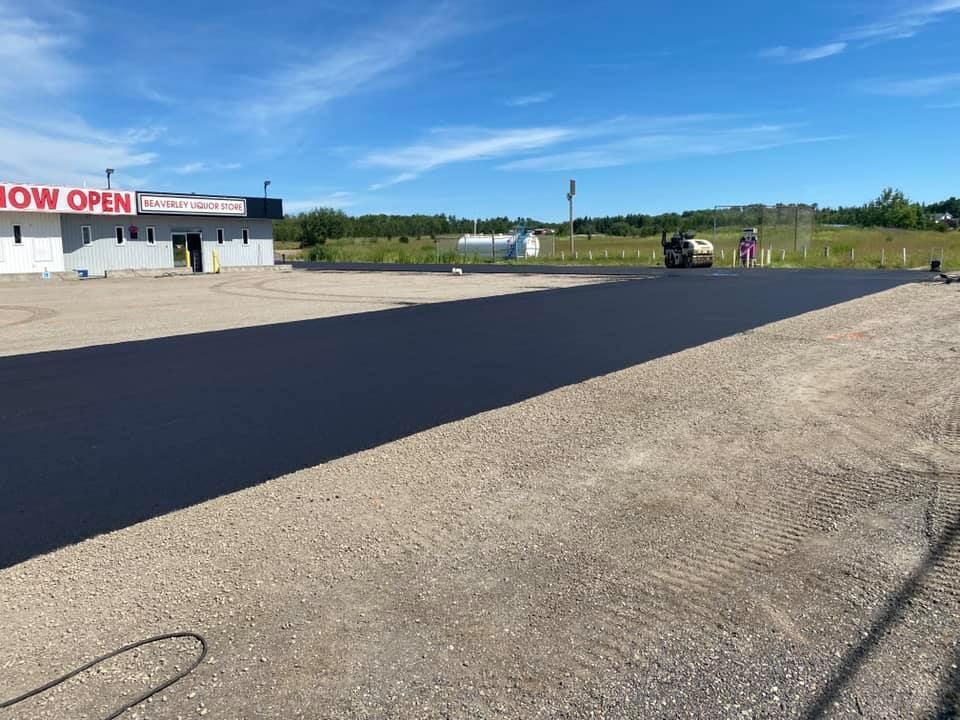 A parking lot is being paved in front of a building that says now open.