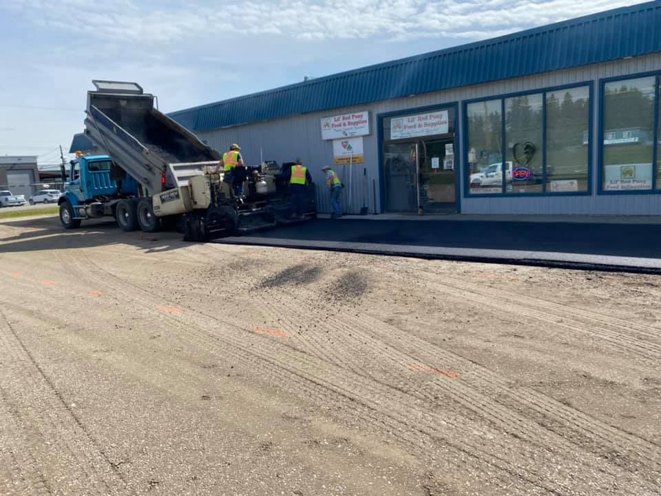 A dump truck is driving down a dirt road in front of a building.