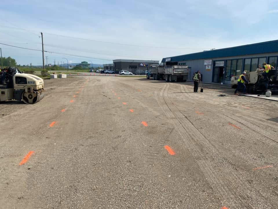 A group of construction workers are working on a road in front of a building.