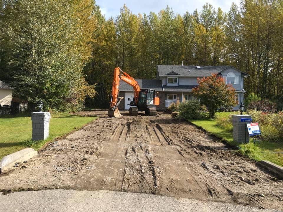 An excavator is working on a dirt road in front of a house.
