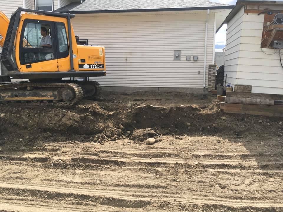 A yellow excavator is digging a hole in front of a house.