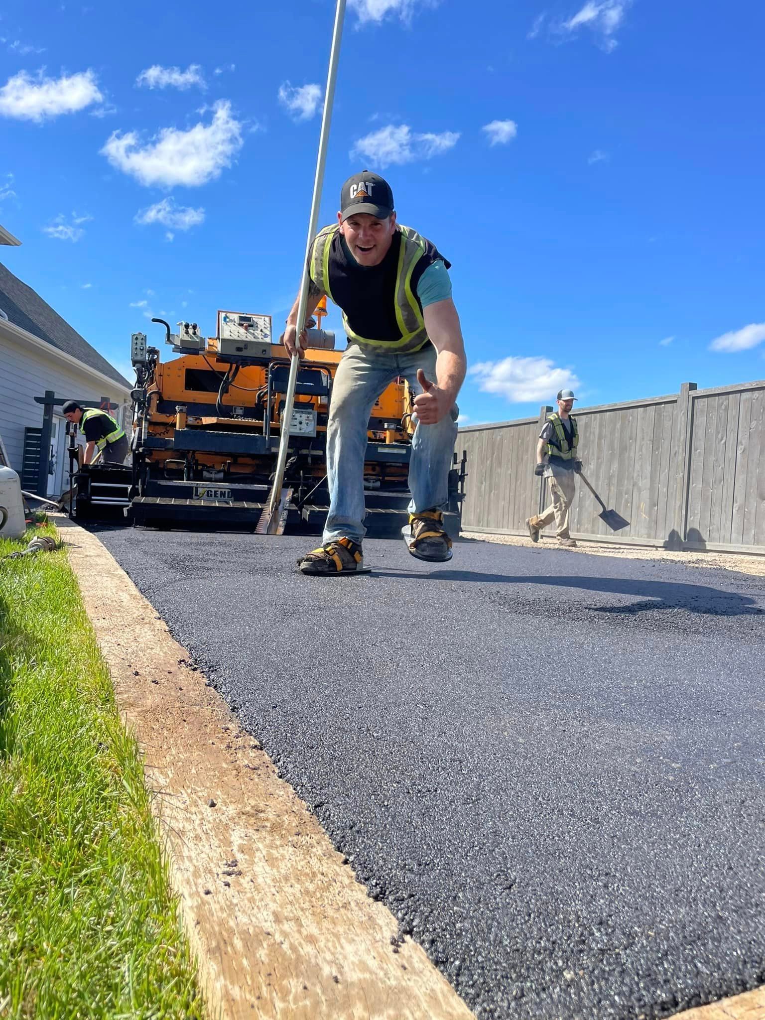 A man is standing next to a machine that is spreading asphalt on a road.