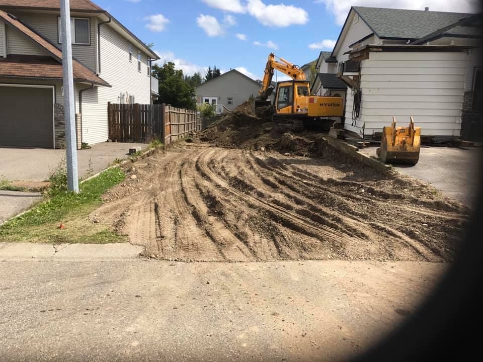 A yellow excavator is moving dirt in front of a house