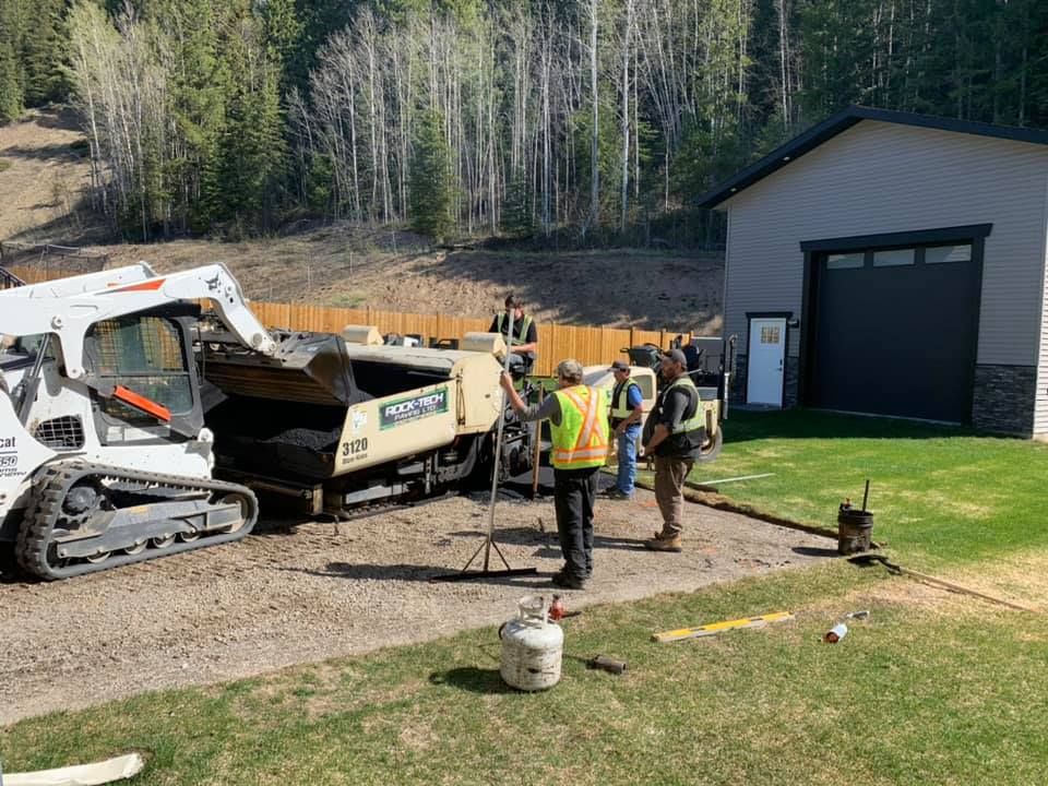 A group of construction workers are working on a driveway in front of a house.