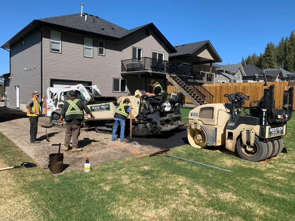 A group of construction workers are working on a driveway in front of a house.