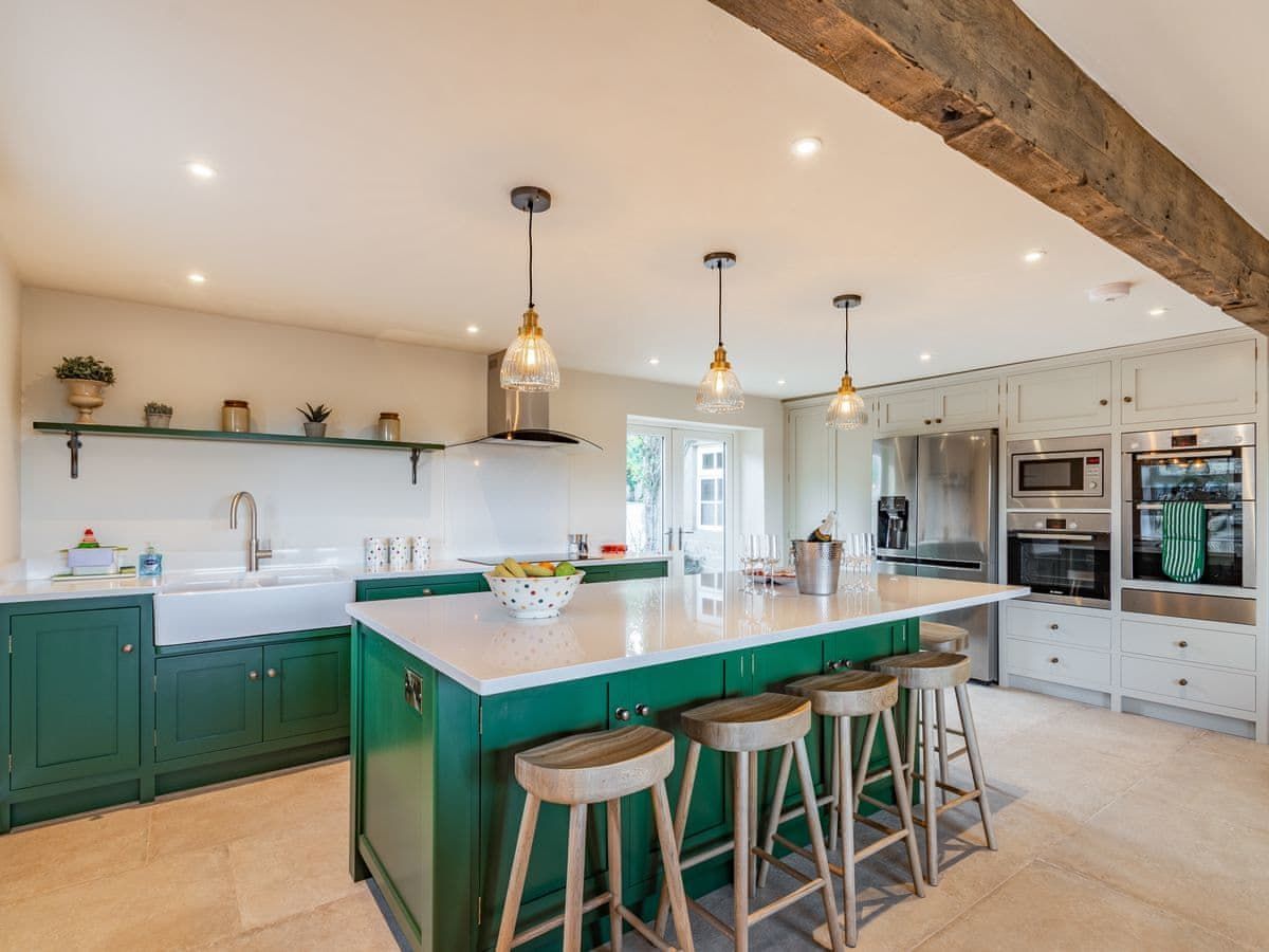 Green and white kitchen with island seating, pendant lights, and stainless steel appliances.