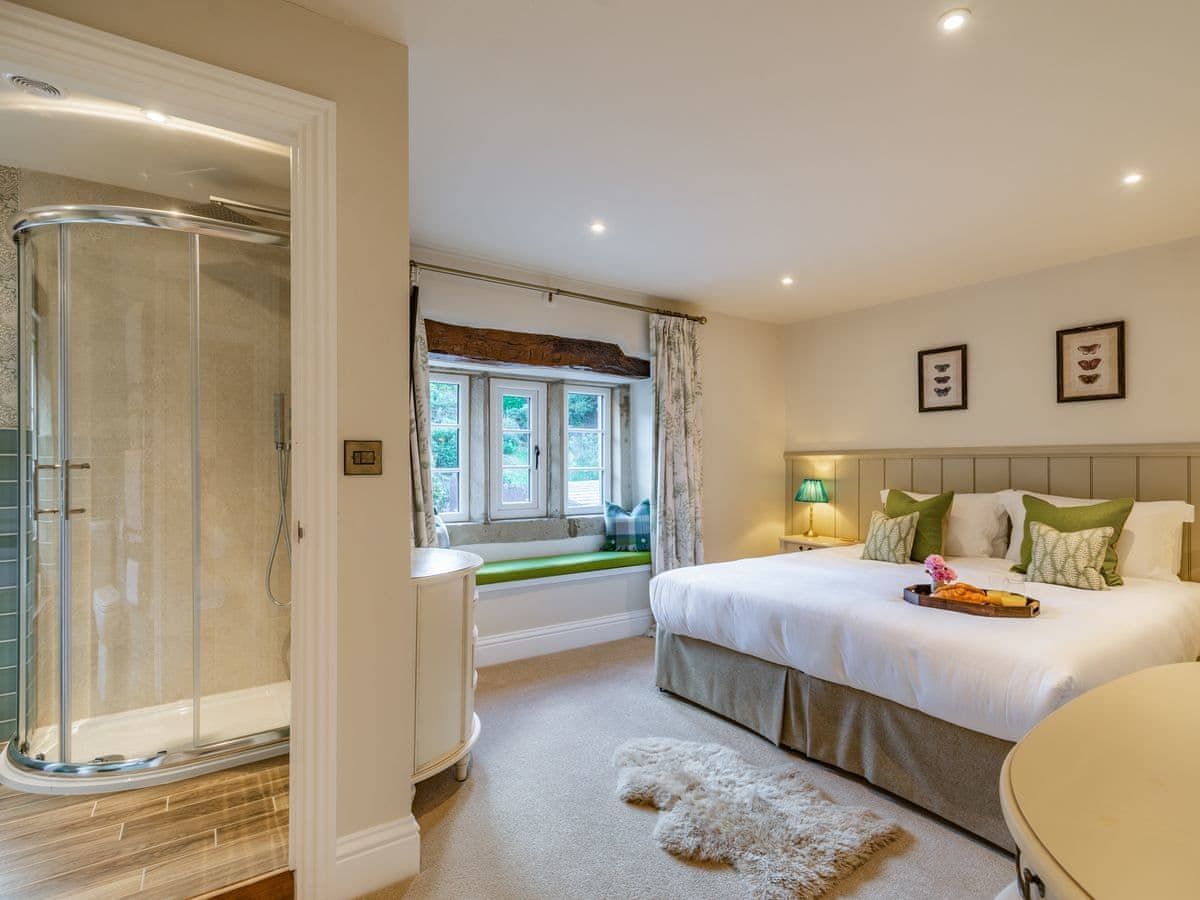 Bedroom with a bed, shower, and window seat. Neutral colors; cream, tan, white, and green. Cozy and well-lit.