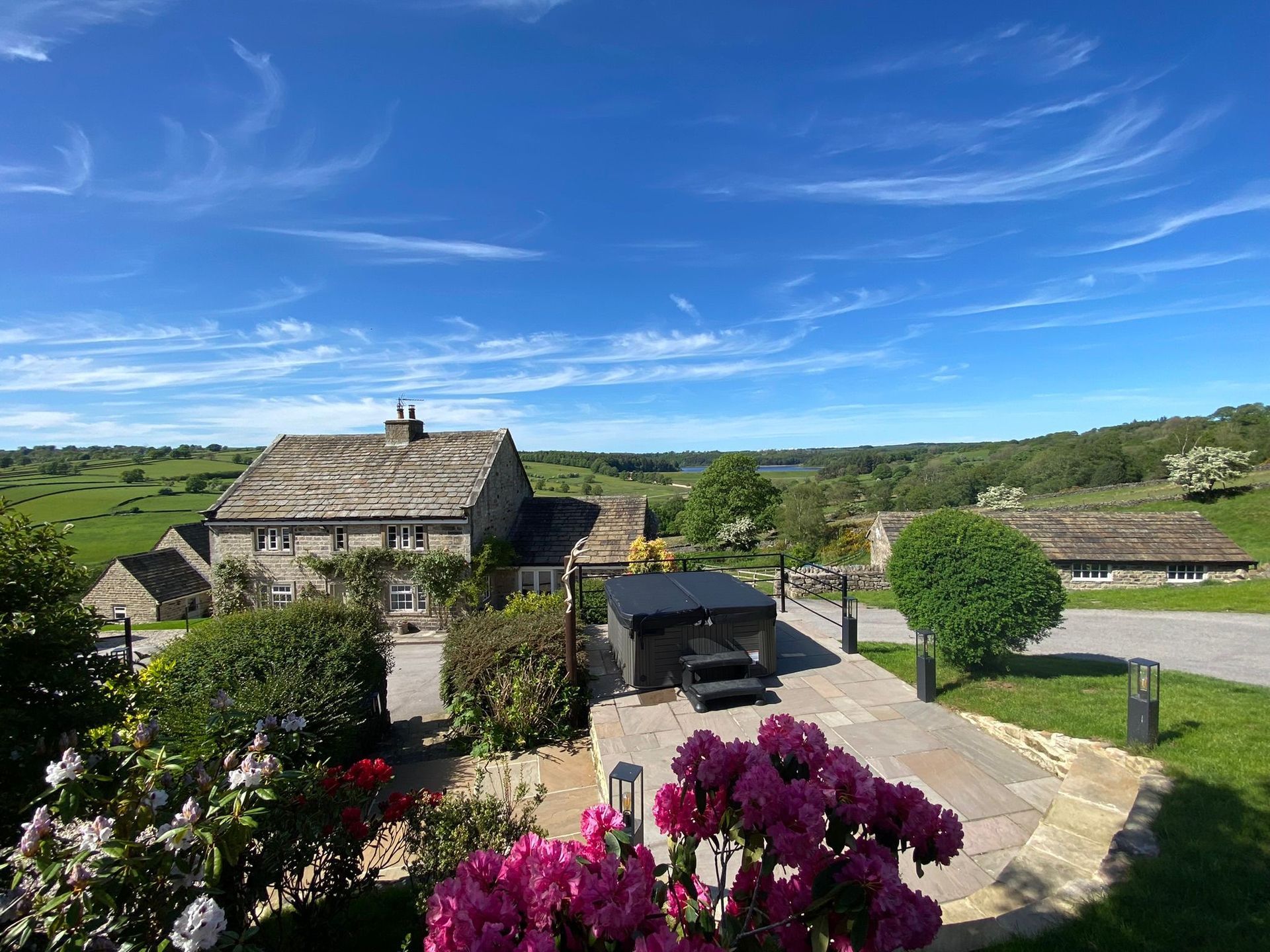 Stone house with a hot tub on a patio, overlooking green fields under a blue sky.