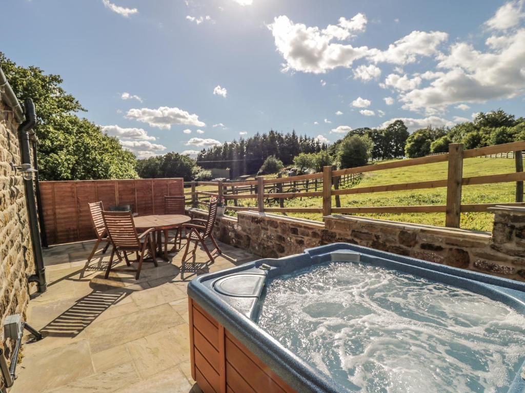Hot tub on a stone patio with outdoor furniture, overlooking a grassy field on a sunny day.