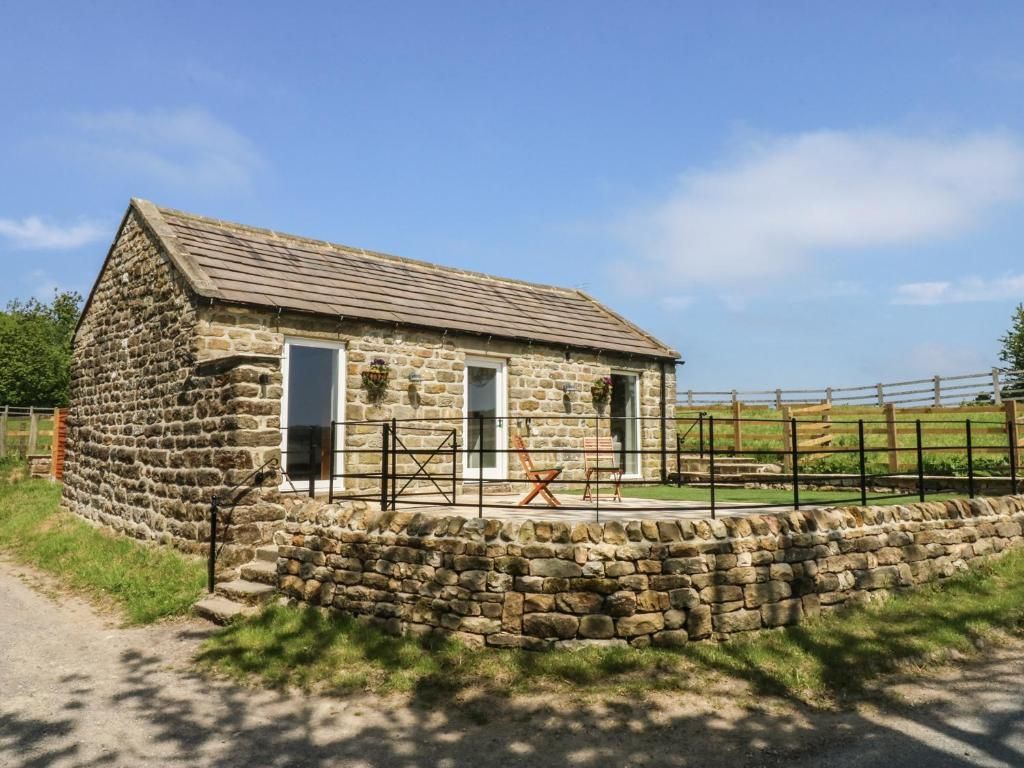 Stone cottage with patio, overlooking a field. Clear blue sky.