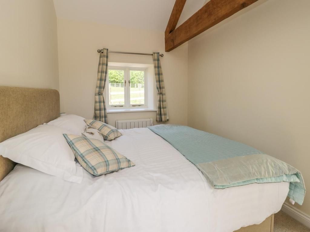 Bedroom with a bed, small window with curtains, and exposed wooden beam.