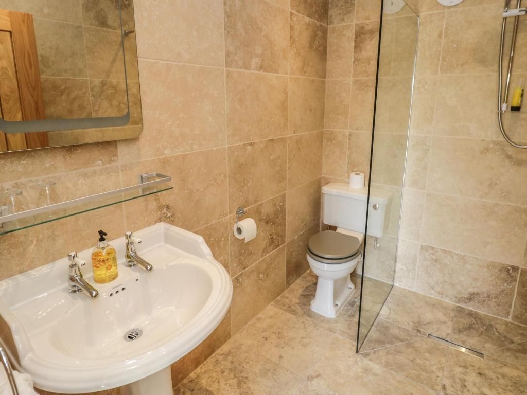 Bathroom with tiled walls, pedestal sink, toilet, and glass shower door.