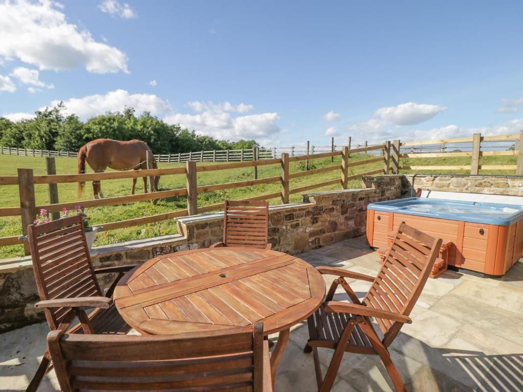 Patio with wooden furniture and hot tub, overlooking a field with a horse.