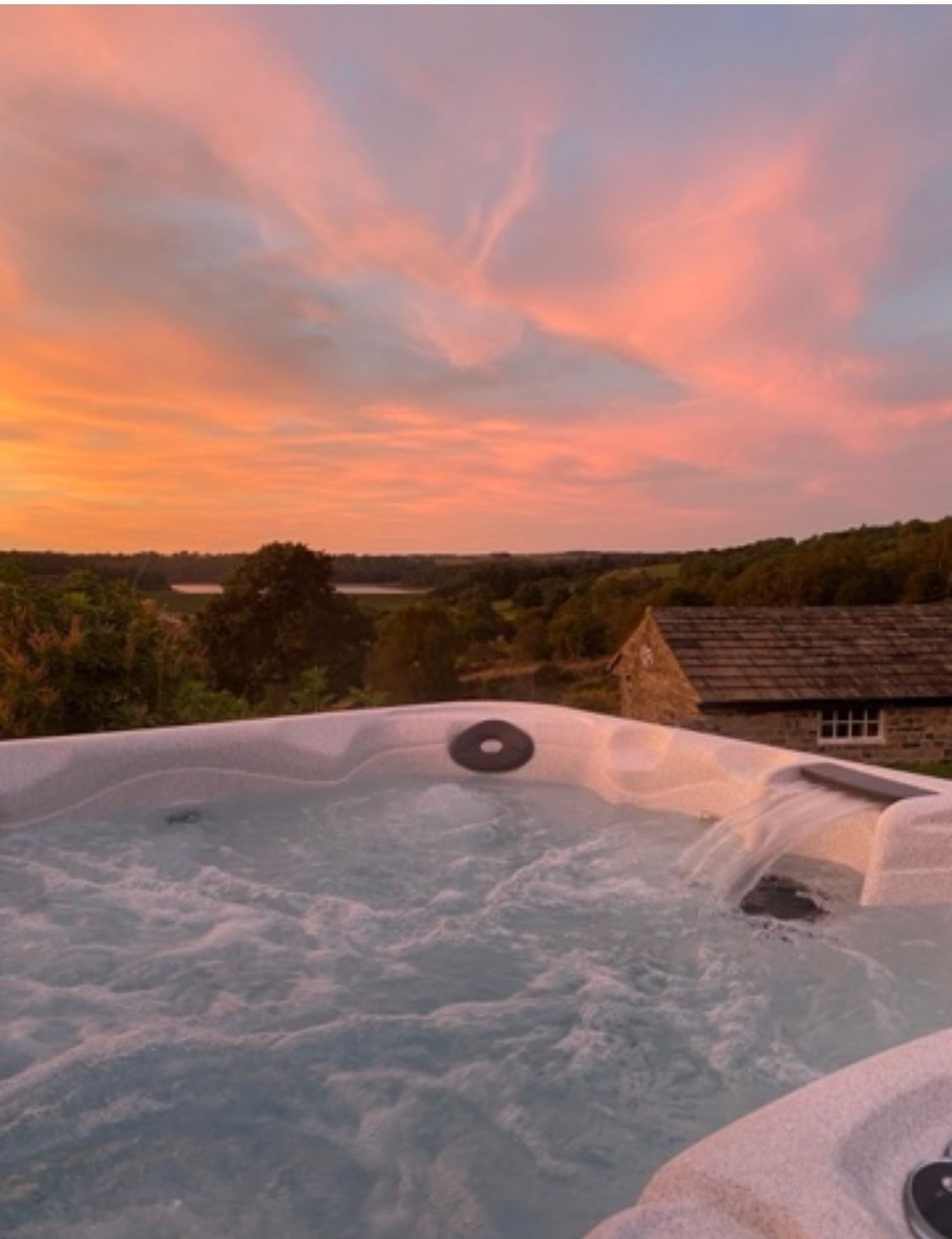 Bubbling hot tub with a view of a sunset sky over a landscape and building.