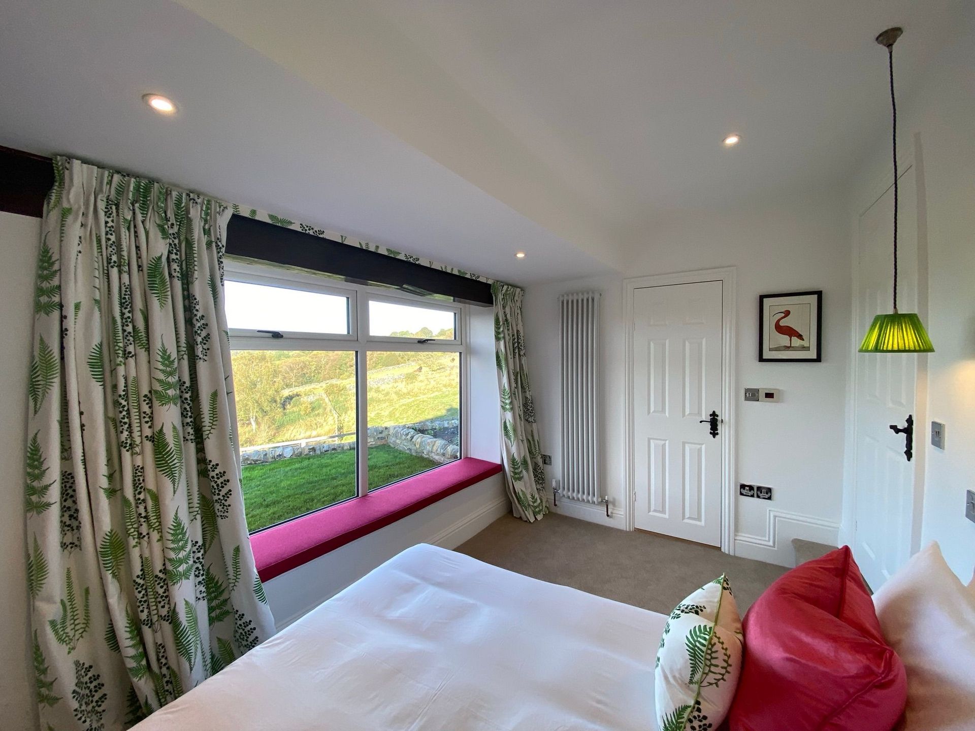 Bedroom with a window seat, green curtains, and a red pillow.