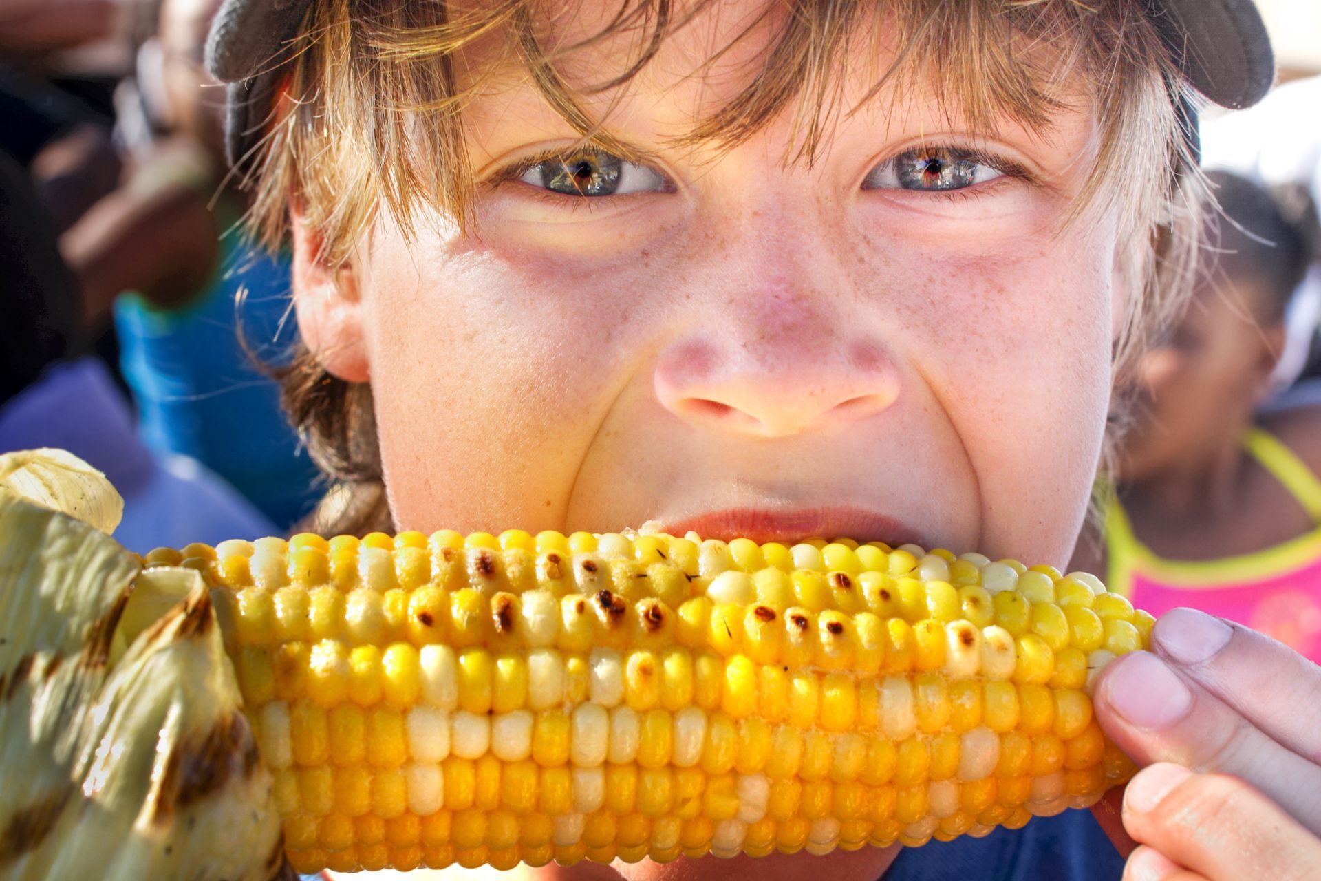 Boy eating grilled corn on the cob, close up. The corn is golden, his expression enthusiastic.