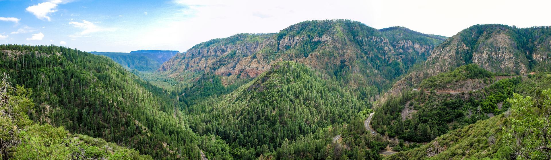 Panoramic view of lush green mountains and a winding road beneath a blue sky.