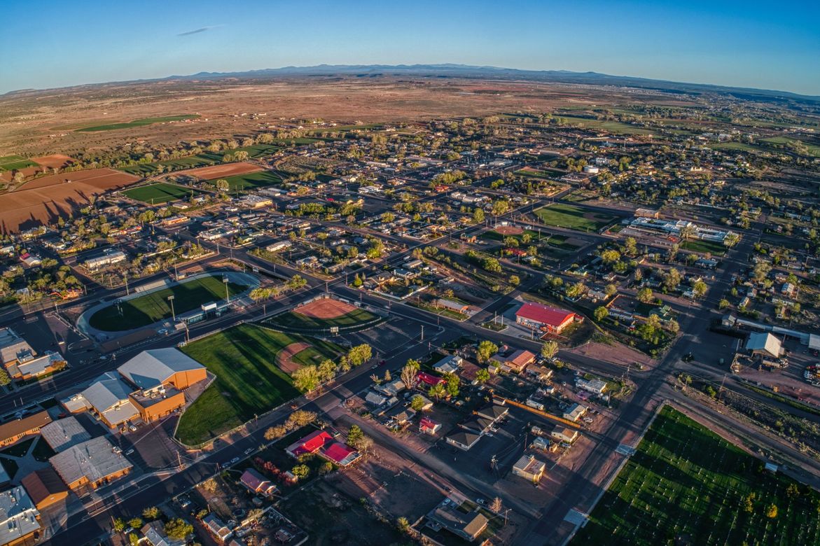 Aerial view of a town with buildings, trees, and fields under a clear blue sky.