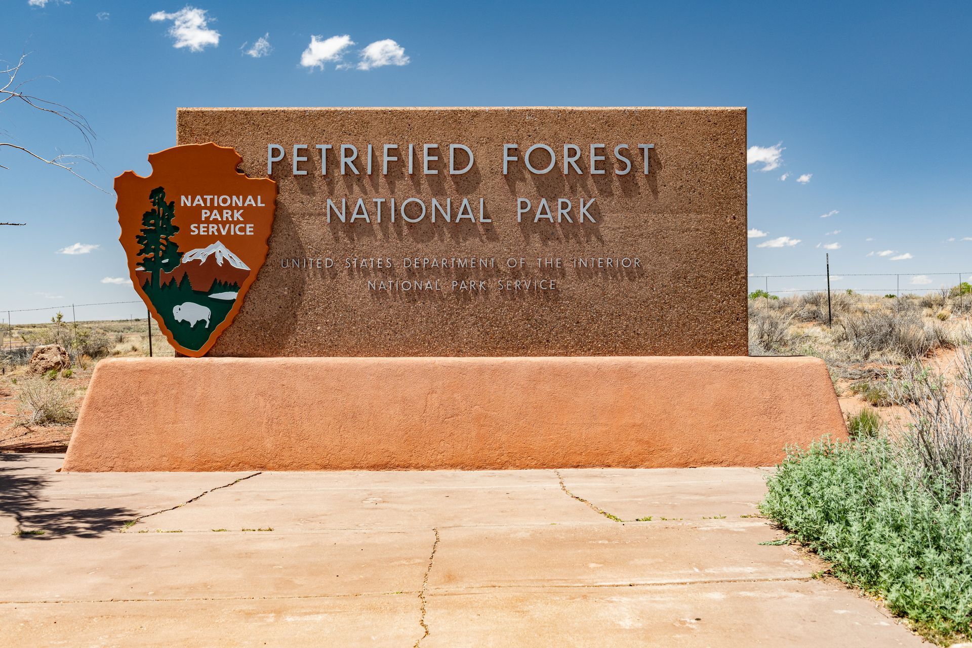 Petrified Forest National Park sign with NPS emblem in the desert under a blue sky.