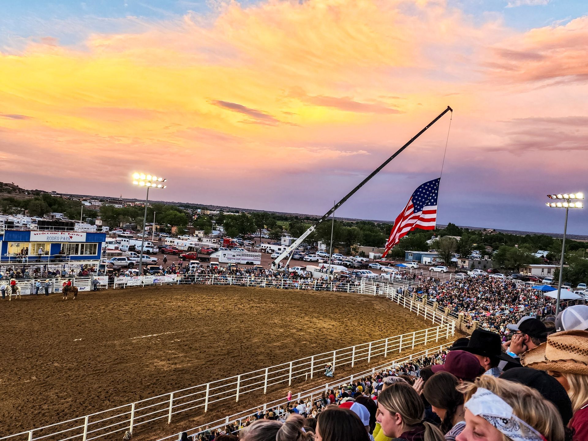 Rodeo arena at sunset with a large crowd, American flag, and crane.