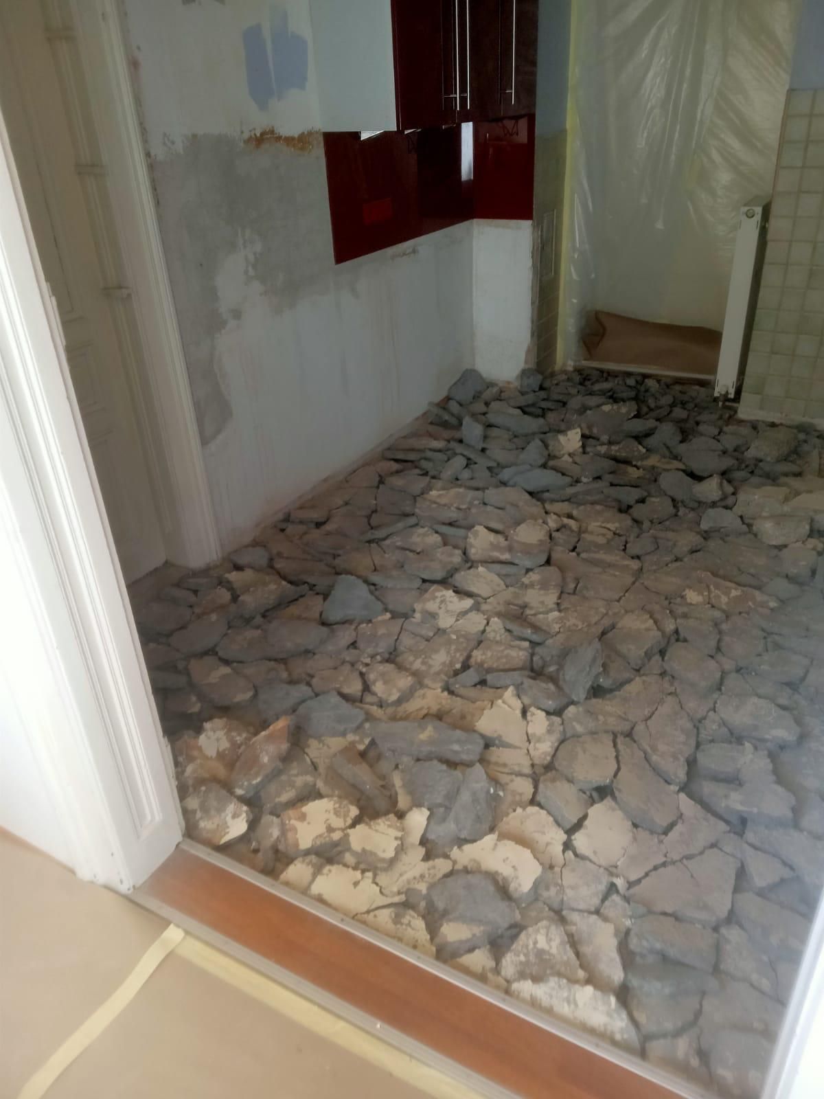 Ein Innenraum, der sich im Umbau befindet und dessen Boden mit losen Betonbrocken und Bauschutt bedeckt ist, ist durch einen Türrahmen zu sehen.