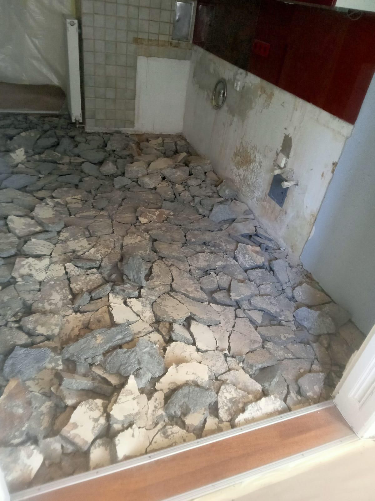 Ein im Bau befindlicher Boden, bedeckt mit Bruchstücken von Steinen und Beton, angrenzend an geflieste und unverputzte Wände.