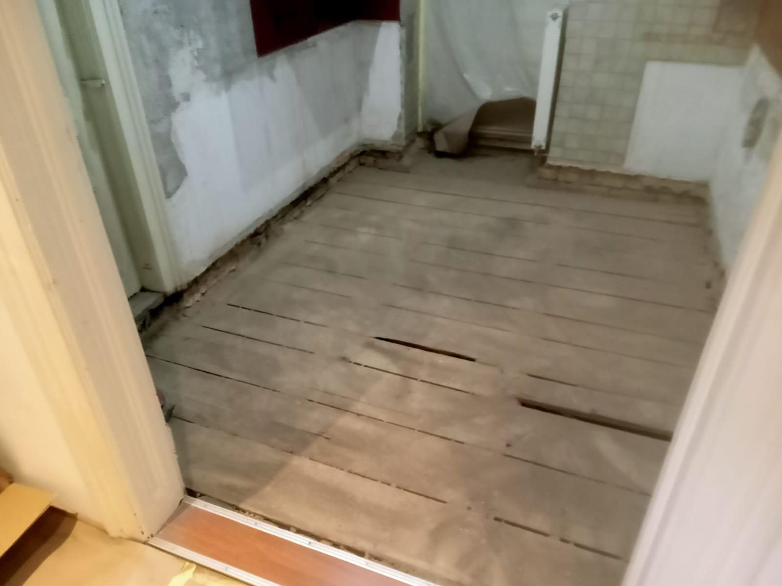 Ein Zimmer im Umbau mit blanken Holzdielen, ungestrichenen Wänden und freiliegenden Kanten in der Nähe der Türöffnungen.