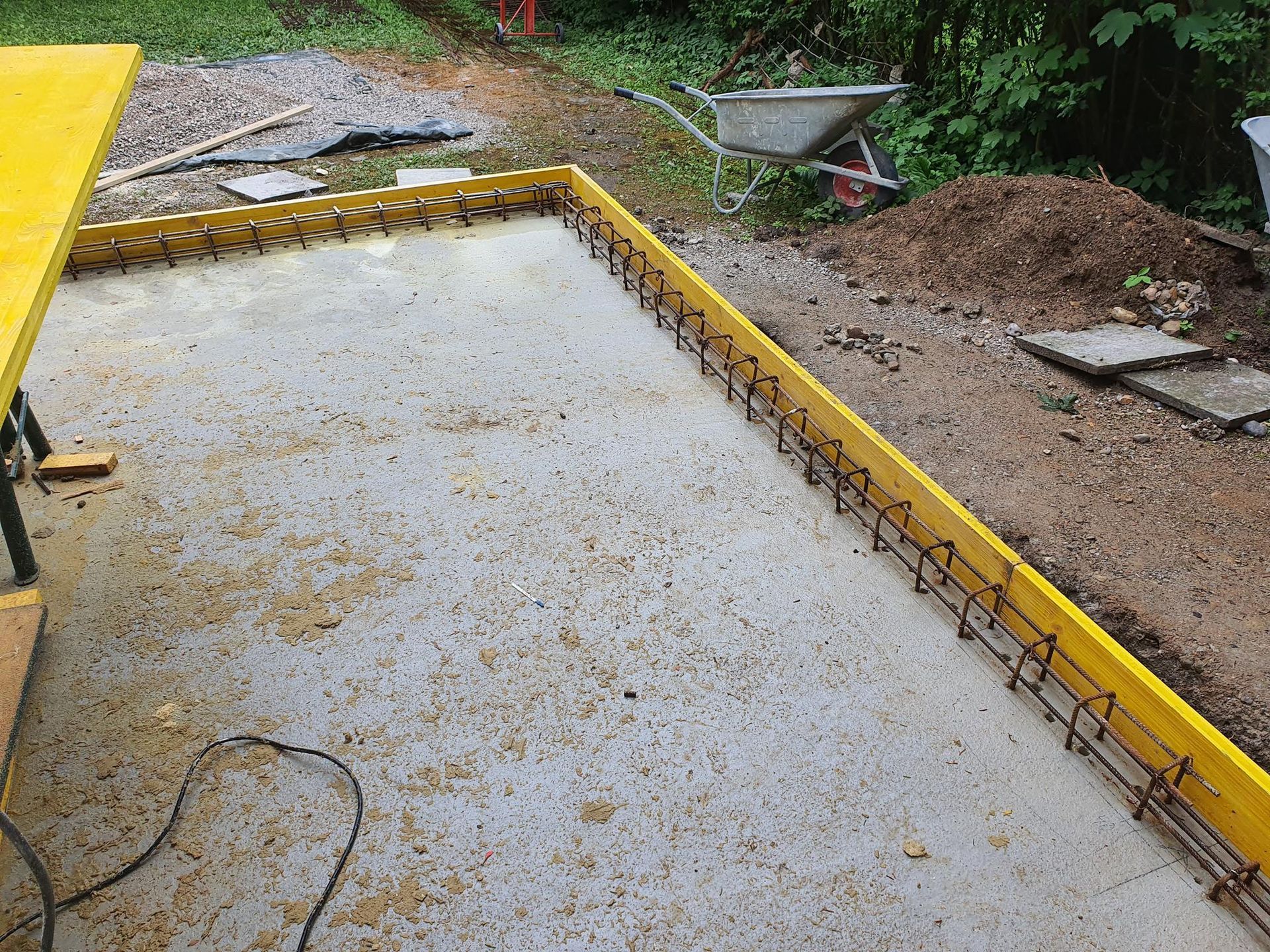Eine mit gelben Holzbrettern und Bewehrungsstahl umrahmte Betonfundamentplatte, im Freien in einem Hof.