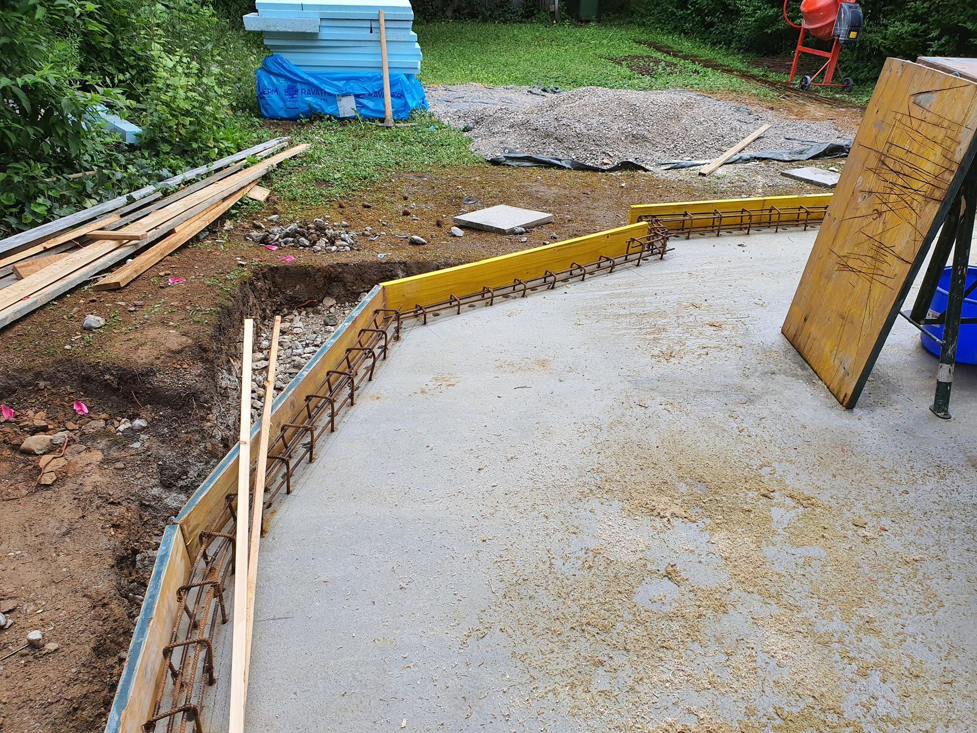 Baustelle mit Betonschalungen, die um den Rand einer Betonplatte herum angebracht sind, wobei Metallarmierungsschlaufen sichtbar sind.