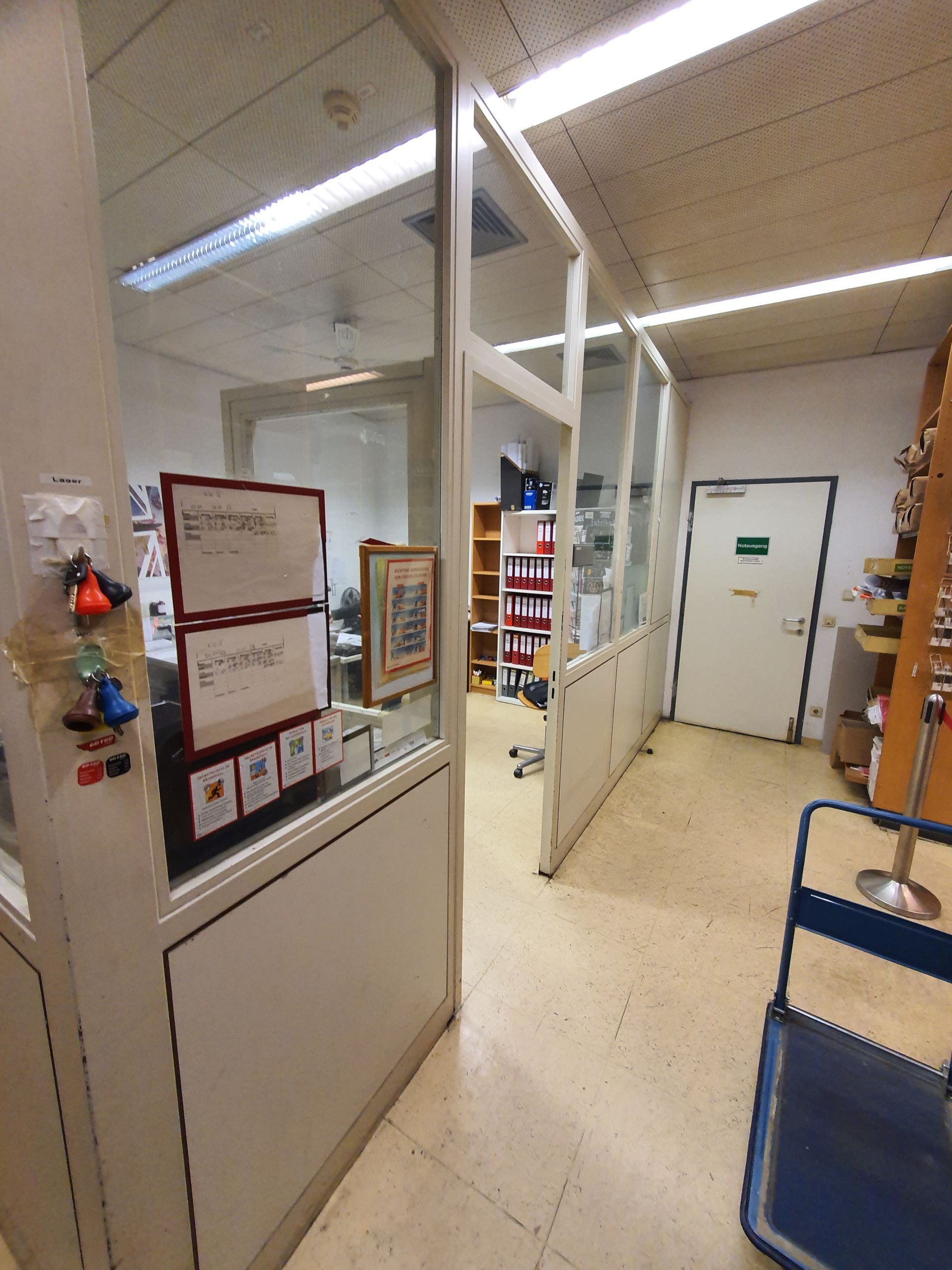 Innenansicht eines Büroeingangs mit einer Glastrennwand, weißen Wänden, einer geschlossenen Tür und einem blauen Wagen.