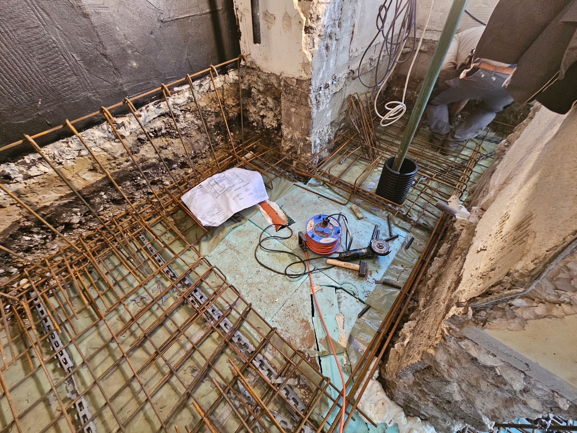 Bauarbeiter verlegen Stahlbewehrungsstahl auf einer Dämmschicht aus Schaumstoff auf einem Betonboden im Inneren eines Gebäudes.