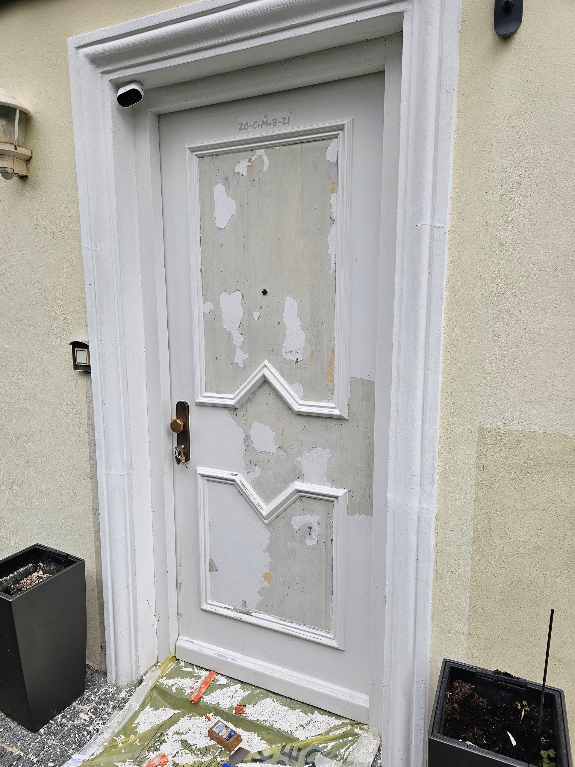 Eine verwitterte weiße Tür mit abblätternder Farbe, die ein V-förmiges Paneelmuster in einer hellen Außenwand aufweist.