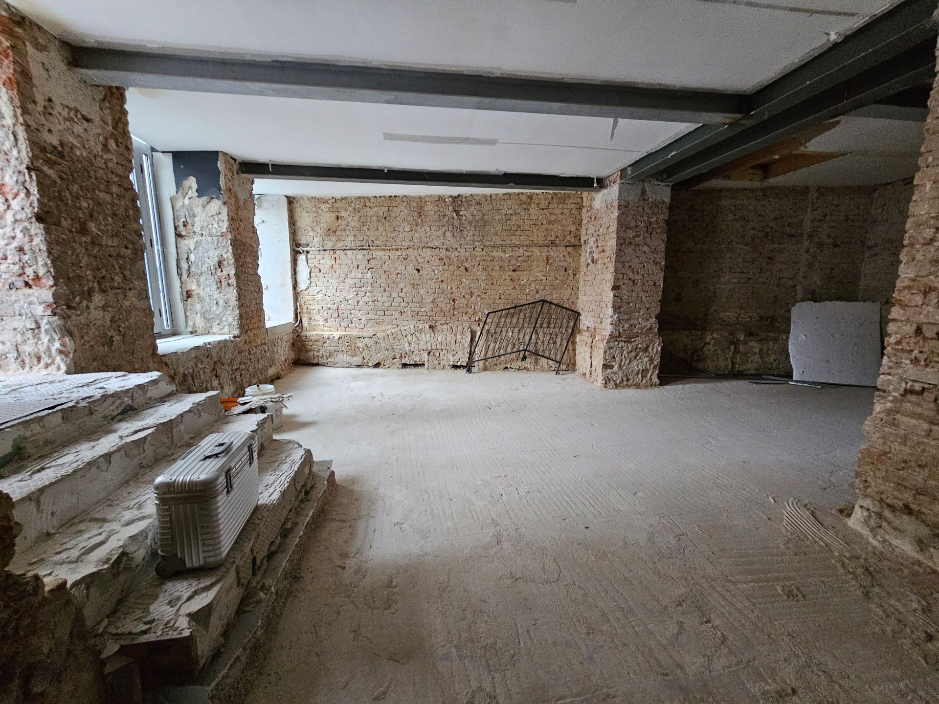 Ein im Bau befindlicher Raum mit freiliegenden Ziegelwänden, einem Betonboden und Stahlträgern, die die Decke stützen.