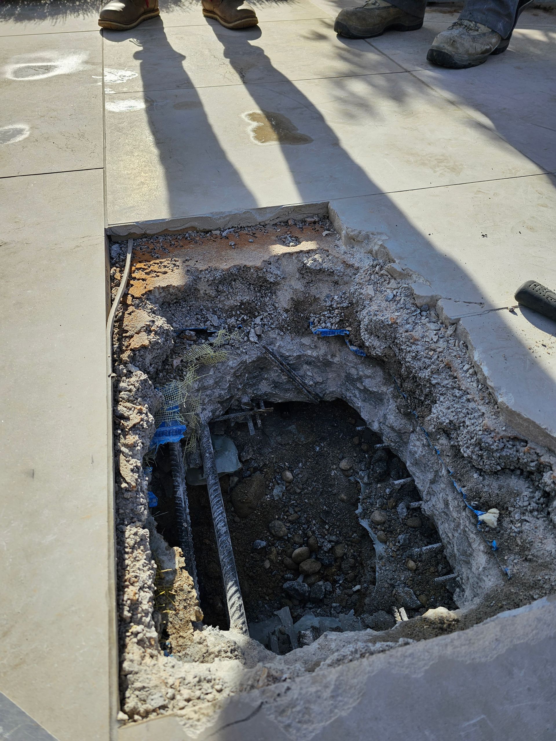 Ein rechteckiges Loch, das in eine Betonoberfläche geschnitten war und darunter liegende Erde und freiliegende Metallbewehrungsstäbe freilegte.