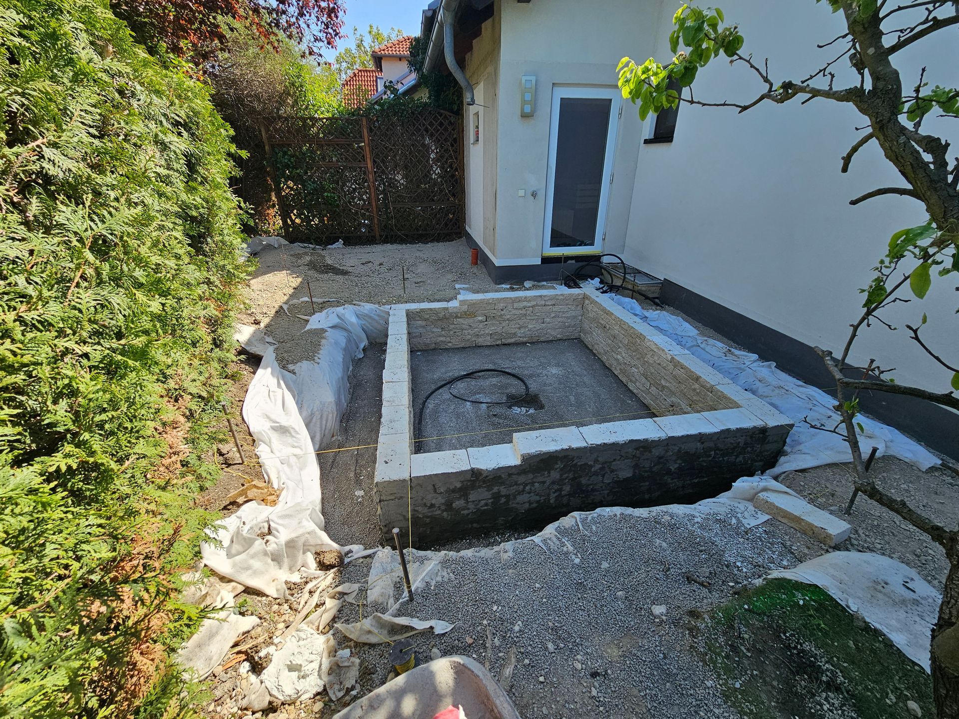 In einem mit Kies gefüllten Hinterhof eines Wohnhauses befindet sich ein im Bau befindliches, rechteckiges Gebäude mit Steinmauern.