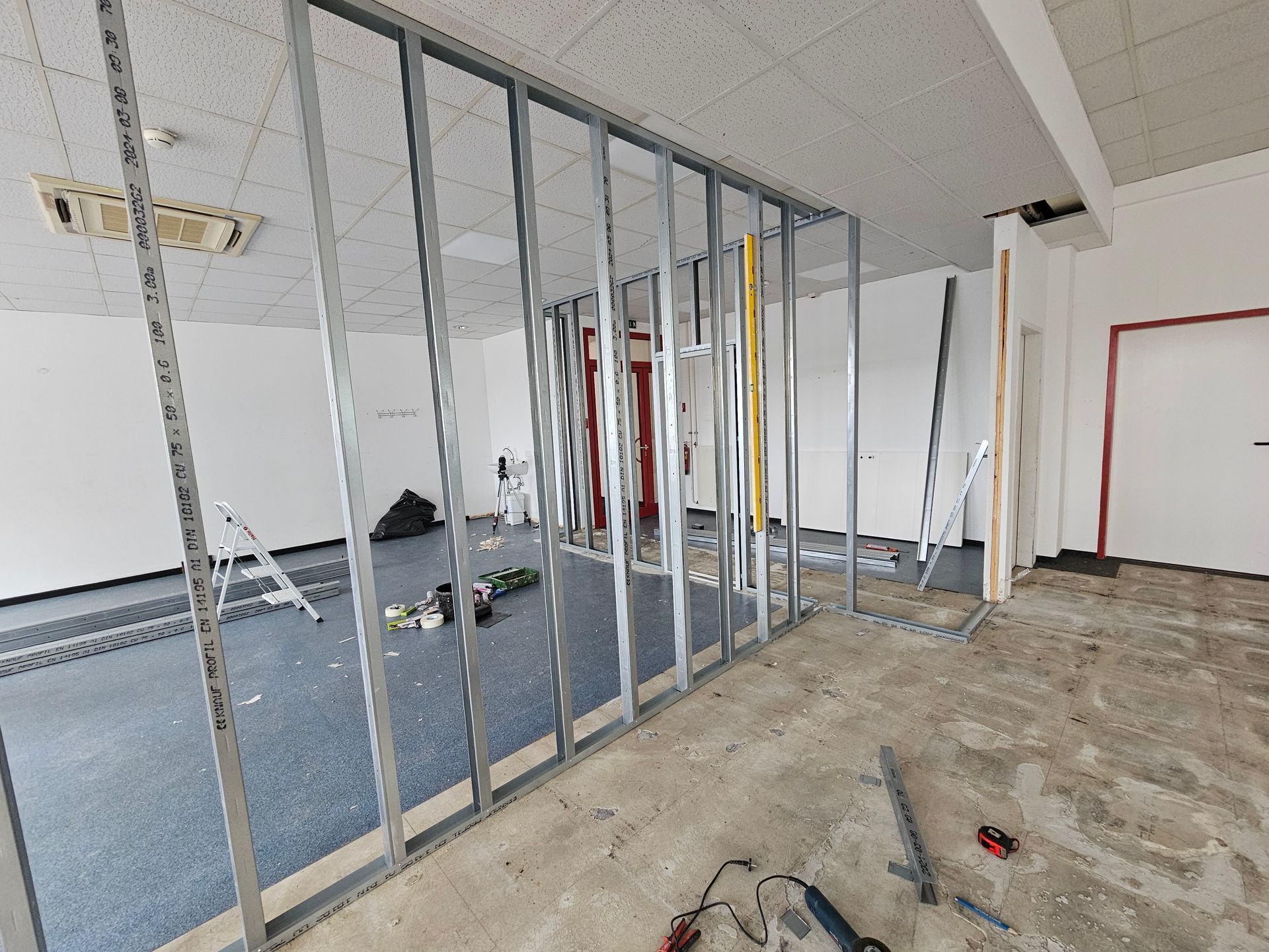 Metallständerkonstruktion für eine Trennwand, die in einem Büroraum mit unfertigem Fußboden und abgehängter Decke installiert wird.