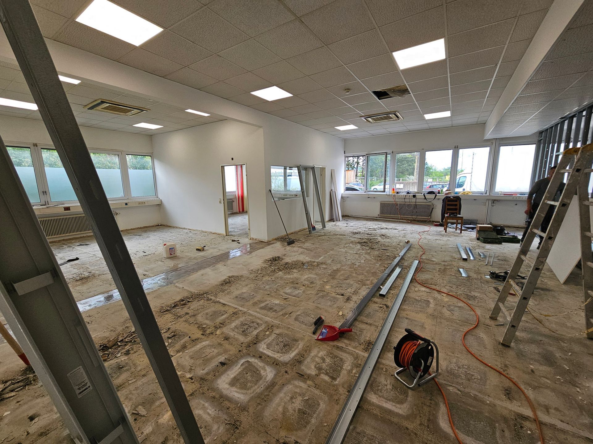 Innenansicht eines im Bau befindlichen Gewerberaums mit freiliegenden Dielenböden, unfertigen Wänden und verstreuten Werkzeugen.