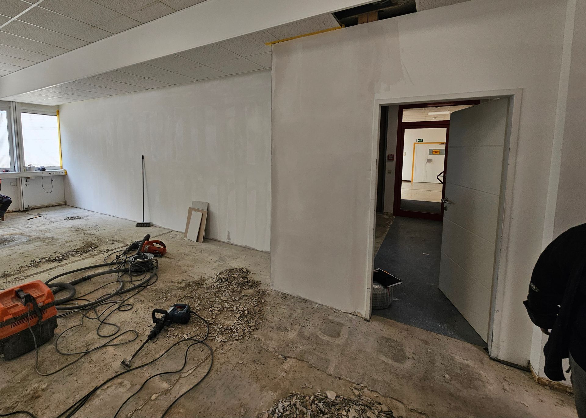 Das Innere einer Baustelle mit frisch verputzten weißen Wänden, einer Tür, die in einen Hinterraum führt, und Bauschutt auf dem Boden.