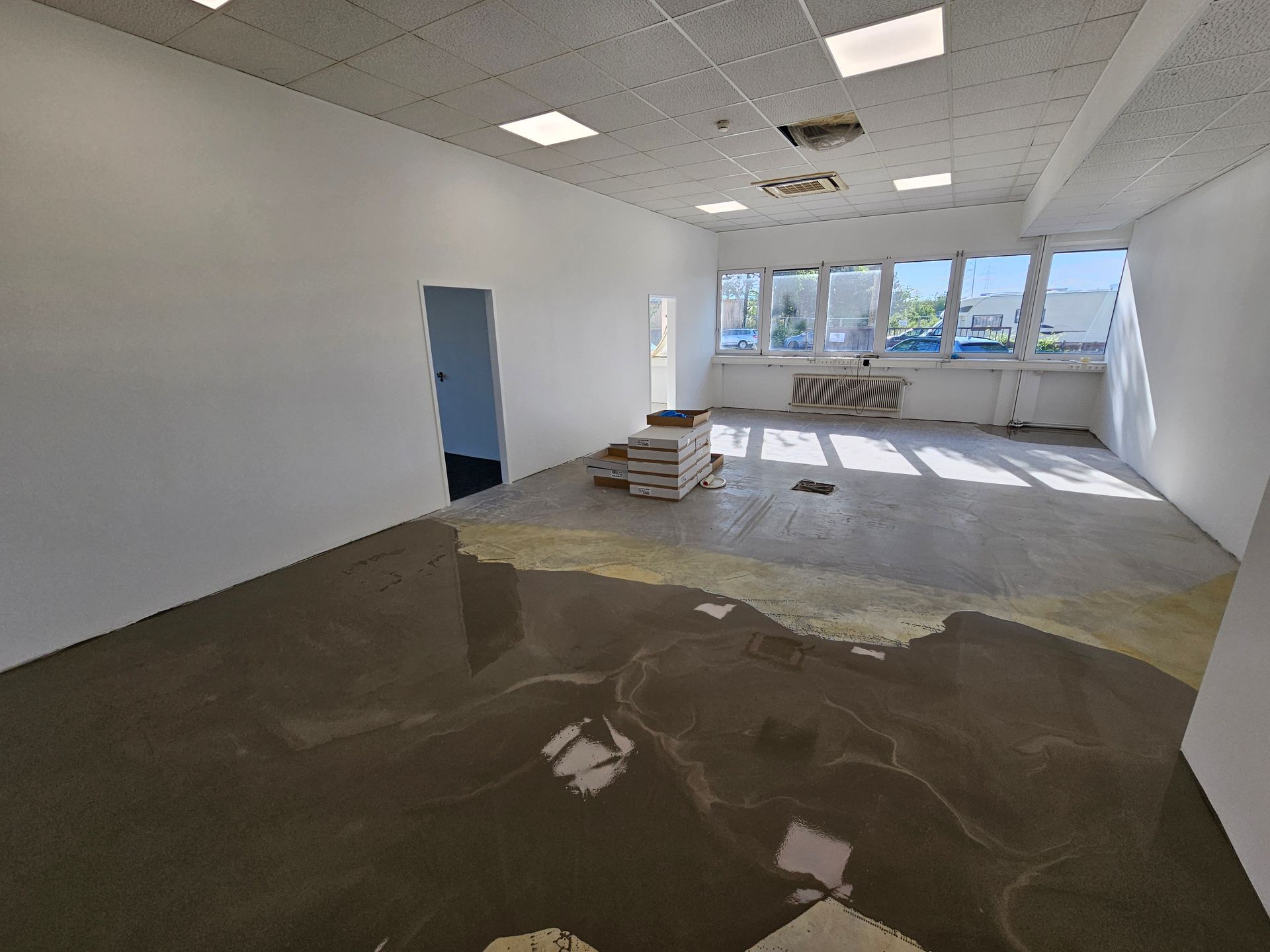 Ein leerstehendes Büro, das derzeit renoviert wird, mit weißen Wänden, einem teilweise fertiggestellten Betonboden und großen Fenstern.