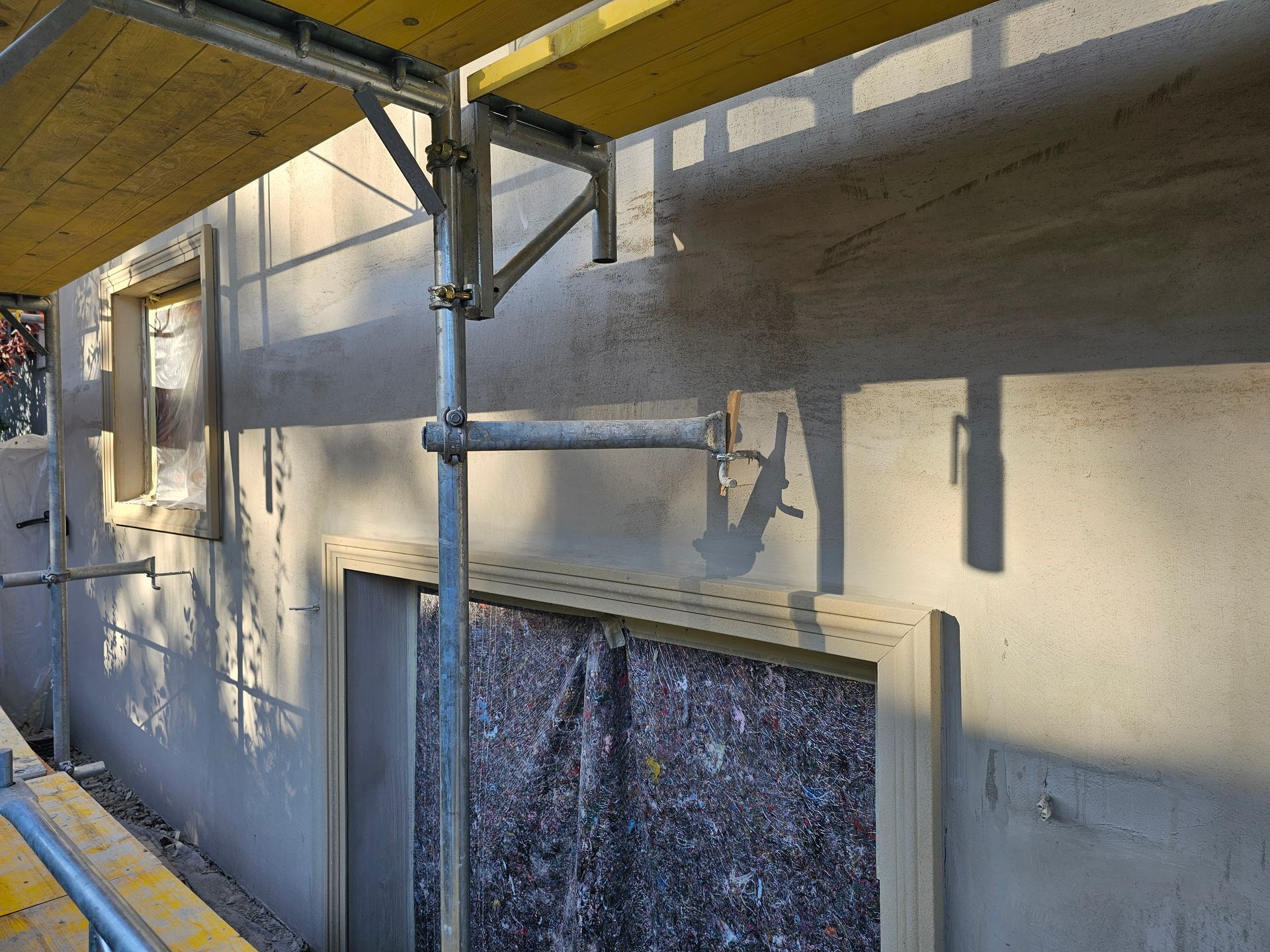 Ein Baugerüst steht vor einer hellgrauen, im Umbau befindlichen Wand, an der die Dämmung im Fensterrahmen freiliegt.