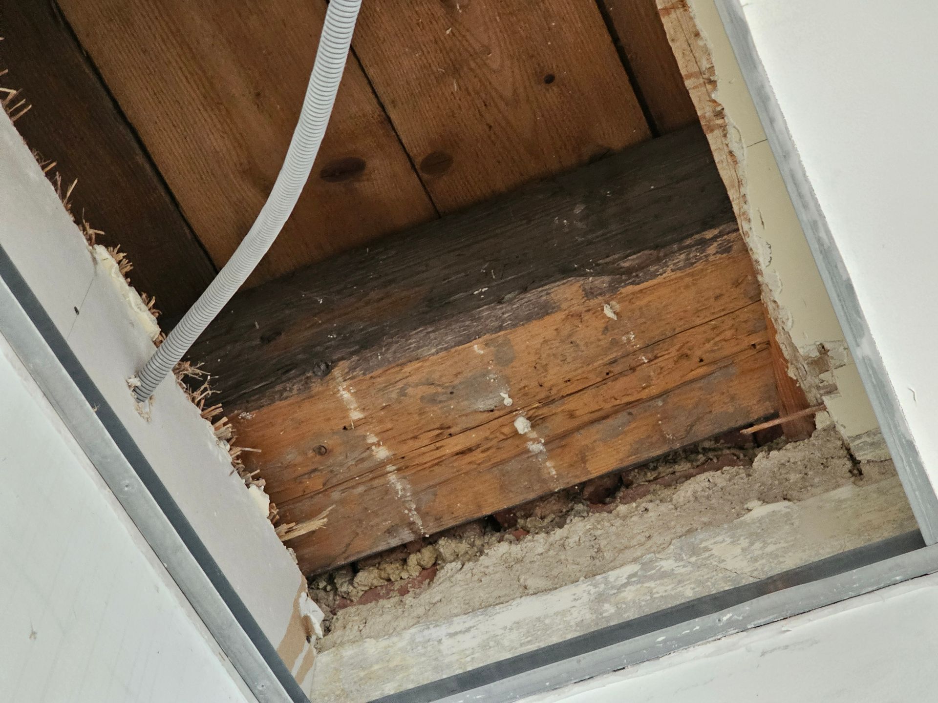 Ein Loch in der weißen Decke gibt den Blick auf hölzerne Bodenbalken und einen darüber liegenden dunklen, verwitterten Tragbalken frei.