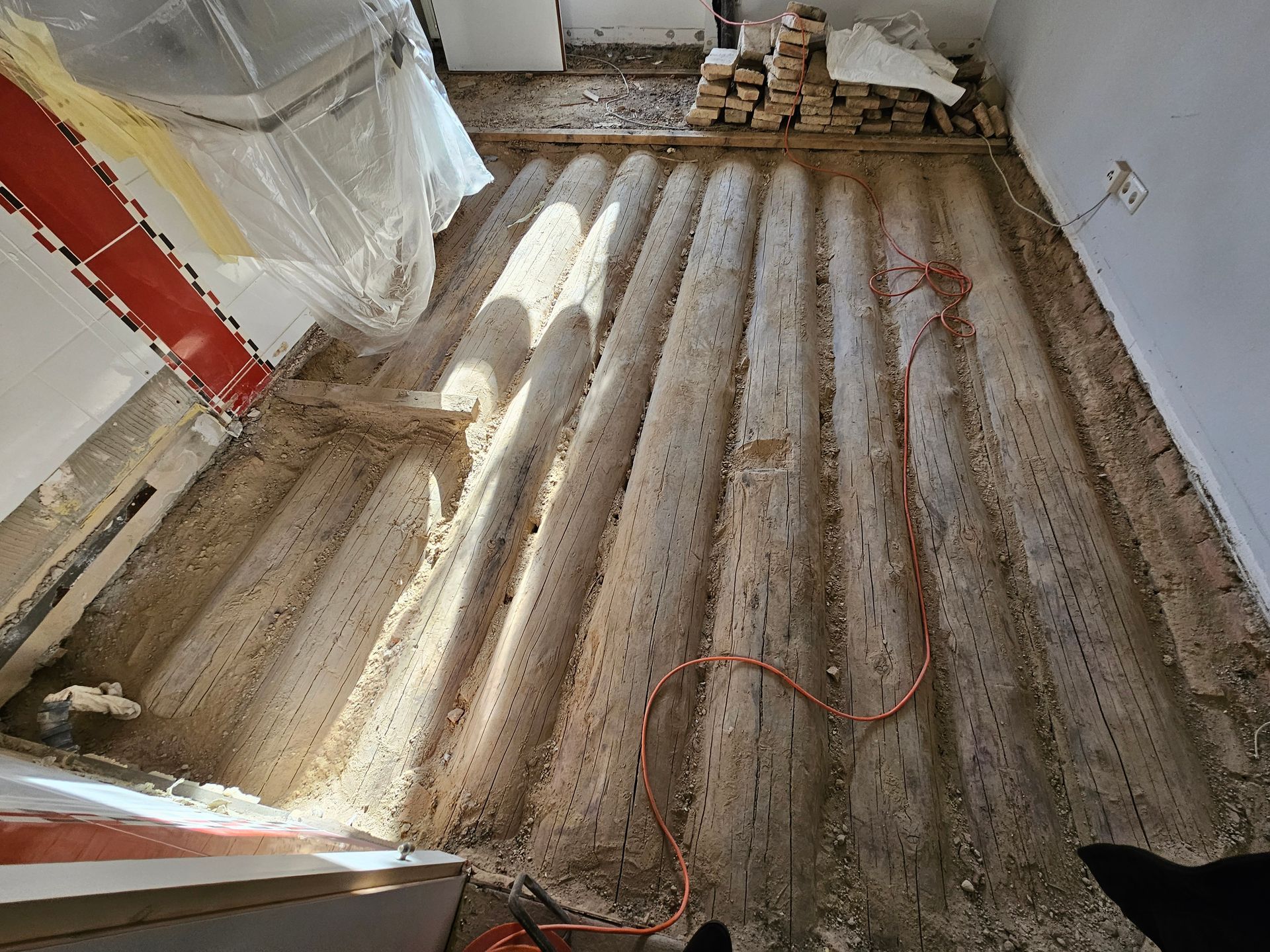 Im Inneren eines Raumes ist ein Unterboden mit freiliegenden, parallel verlaufenden Wellblechträgern und Bauschutt zu sehen.