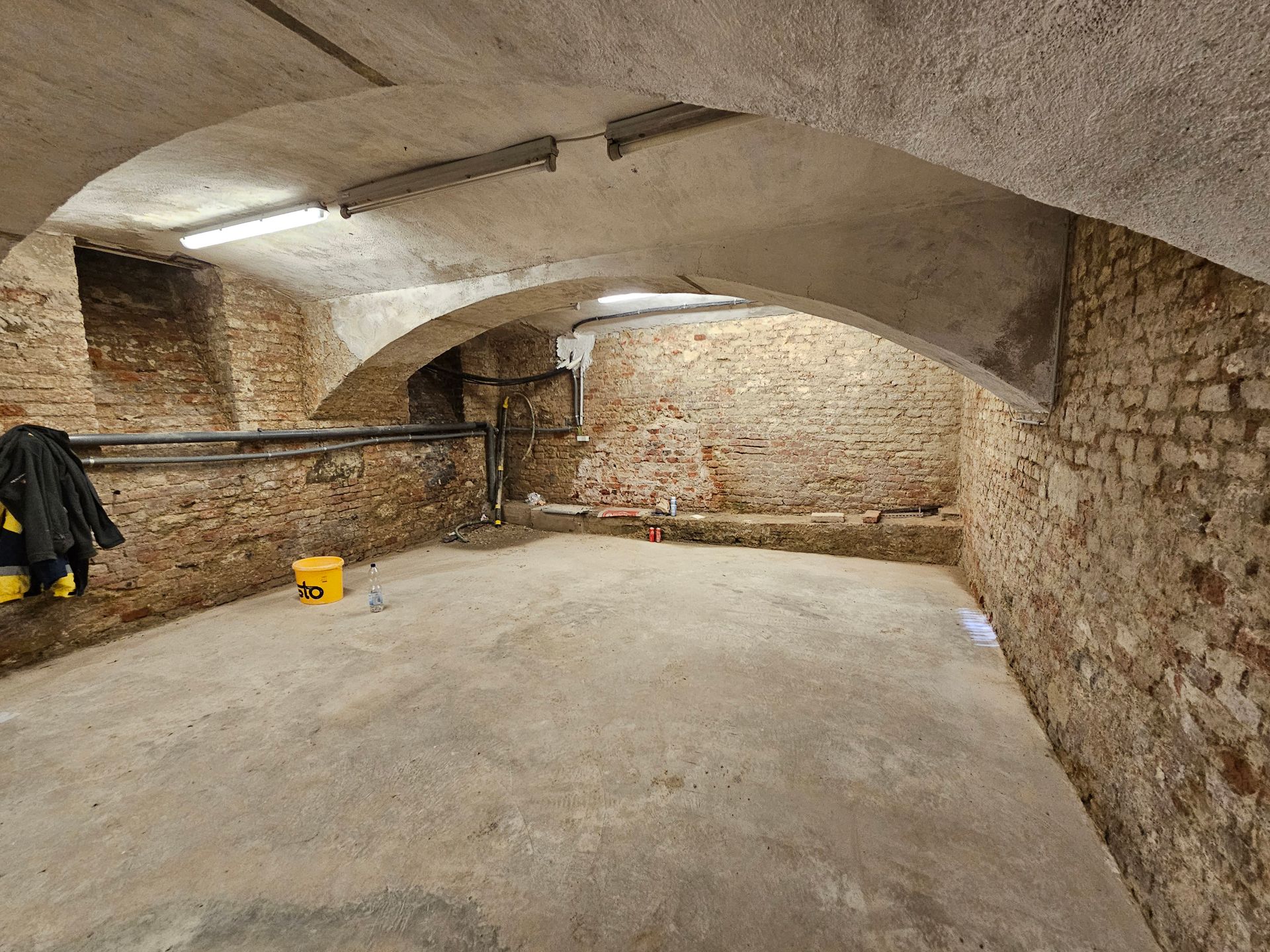 Ein leerer Steinkeller mit gewölbter Decke und Betonboden.