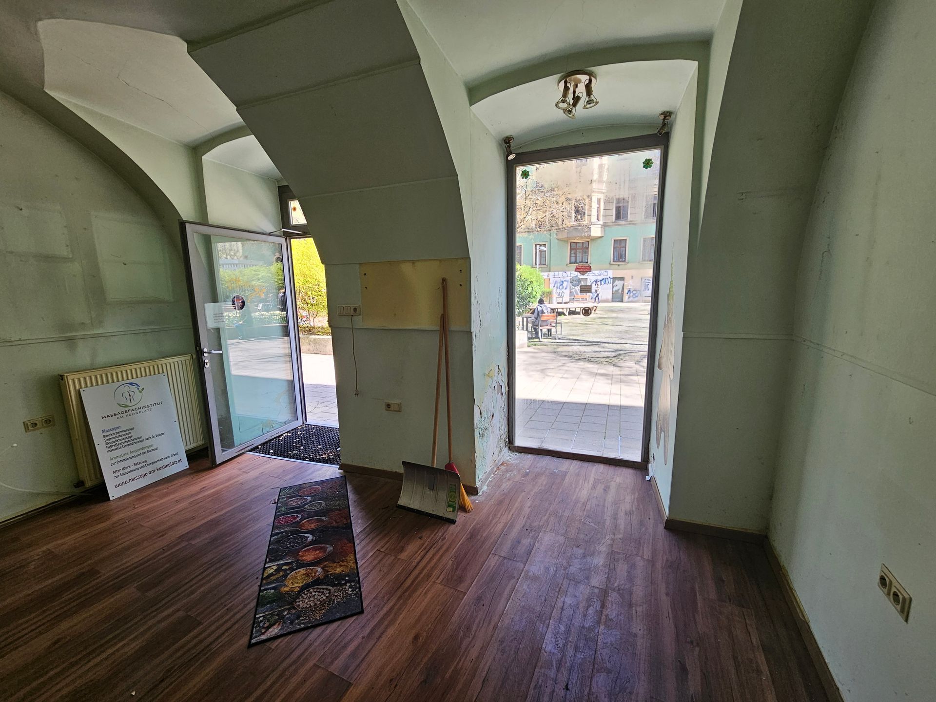 Innenansicht eines Zimmers mit gewölbten Decken, Holzböden, zwei offenen Glastüren und einem an der Wand lehnenden Besen.