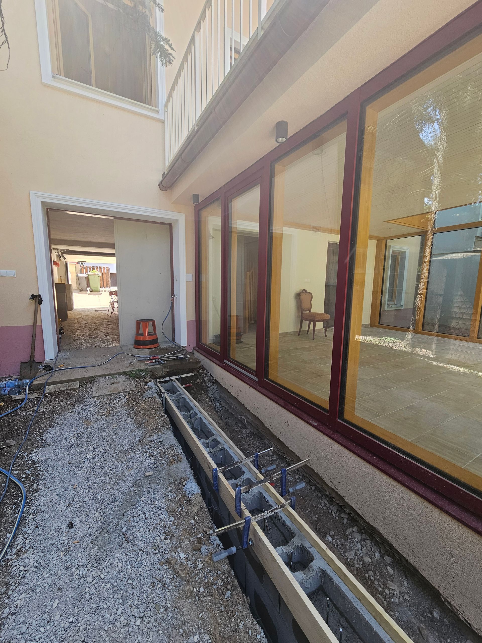 Eine Baustelle vor einem Gebäude mit großen Glasfenstern, auf deren Hof eine Betonfundamentschalung zu sehen ist.