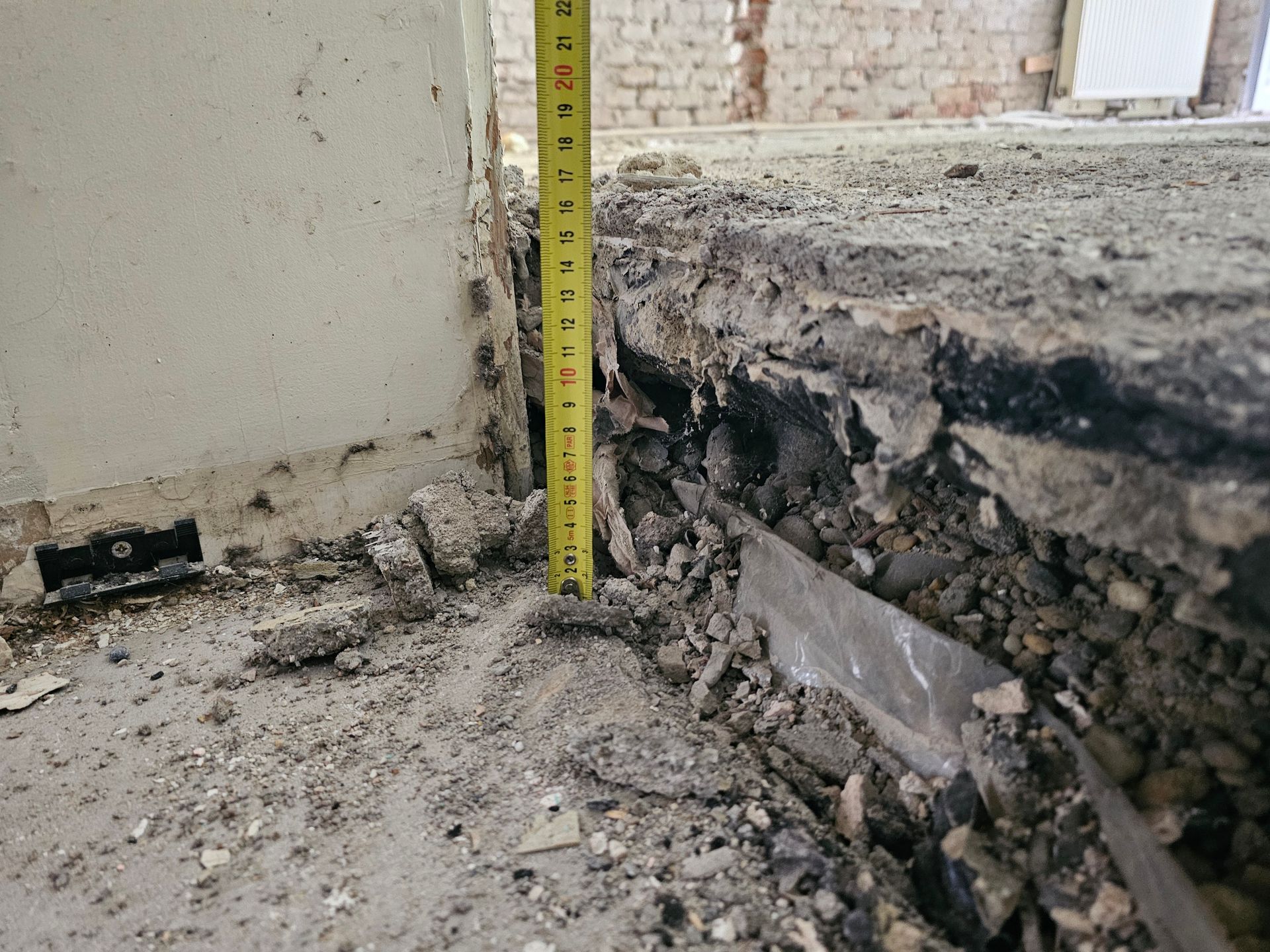 Auf einer Baustelle oder bei einer Renovierung lehnt ein gelbes Maßband senkrecht an einer beschädigten Betonbodenkante.